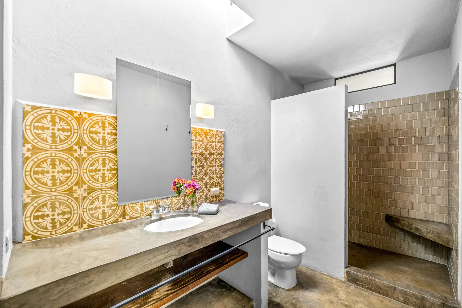 Casa Beatrice, bathroom with a patterned yellow tile wall, a mirror, a vessel sink with flowers, a toilet and a tiled shower, San Miguel de Allende