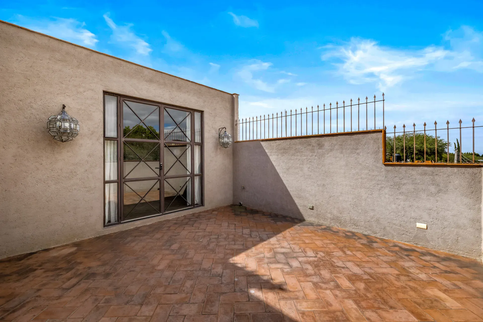Casa Beatrice, empty roof terrace with a steel-framed glass door, two lanterns and a wrought-iron fence, San Miguel de Allende