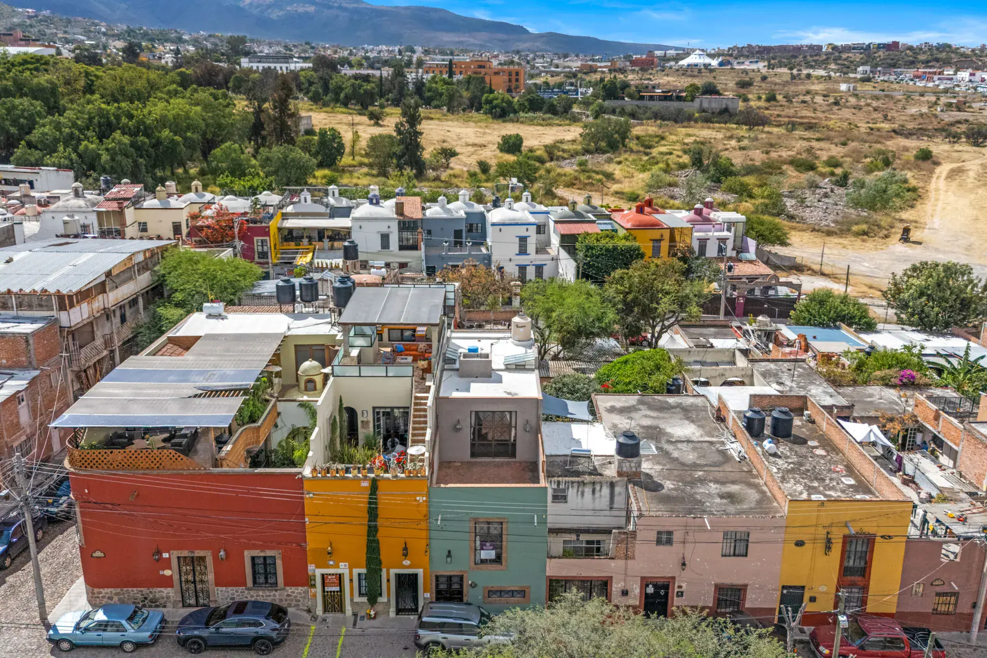 Casa Beatrice, aerial view of the colorful row of houses along the street with a rooftop terrace and open land beyond, San Miguel de Allende