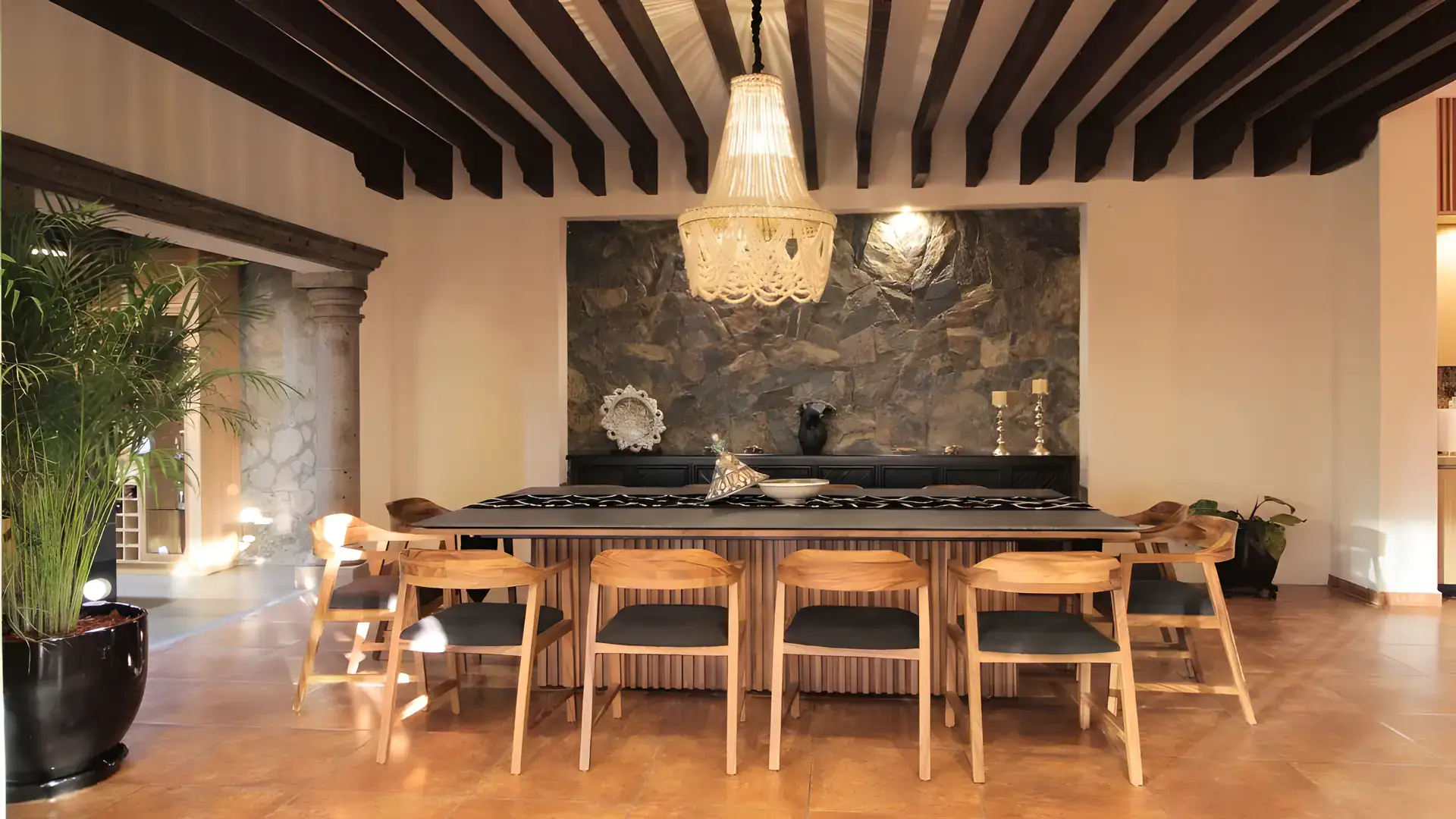 Casa Bellavista, dining area with a long table, wood chairs, a stone feature wall and a beaded chandelier under a beamed ceiling, San Miguel de Allende