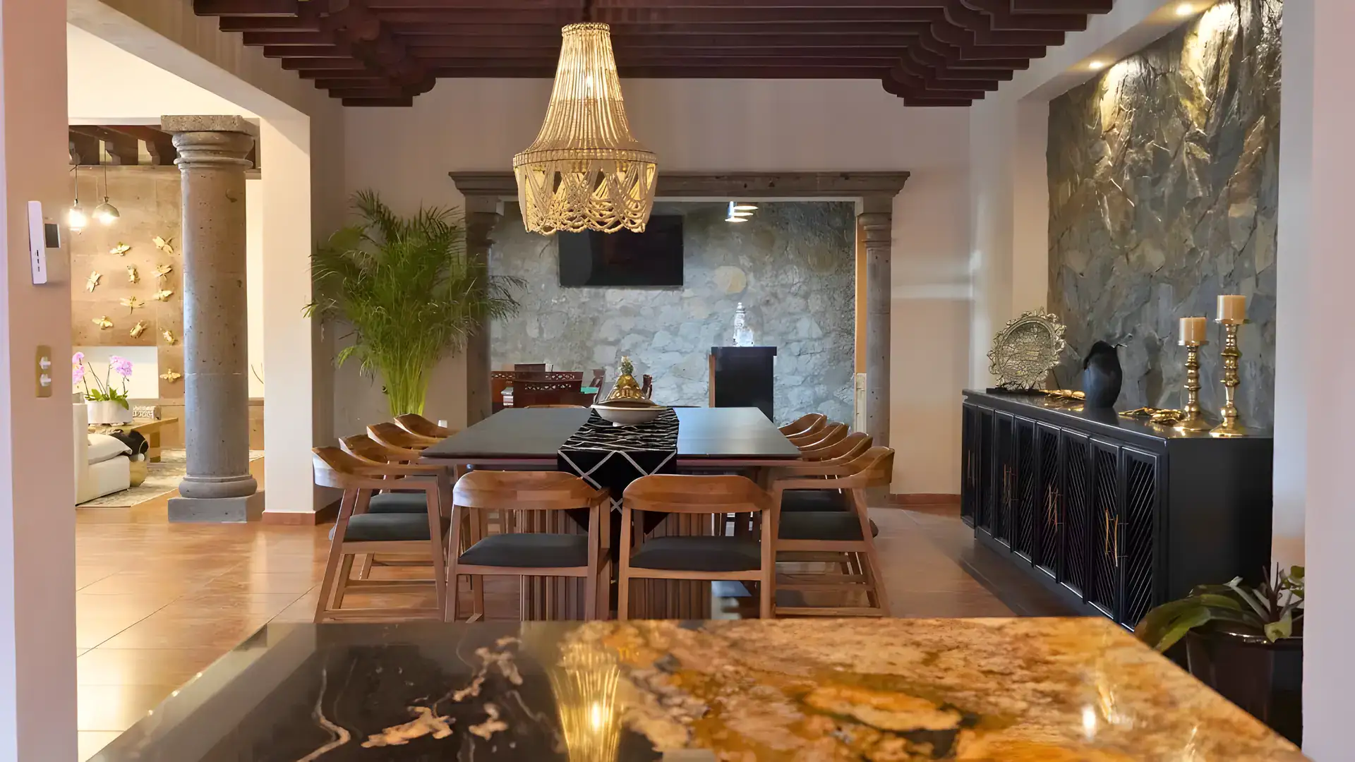 Casa Bellavista, dining room with stone columns, a stone fireplace wall with a television and a black sideboard, San Miguel de Allende