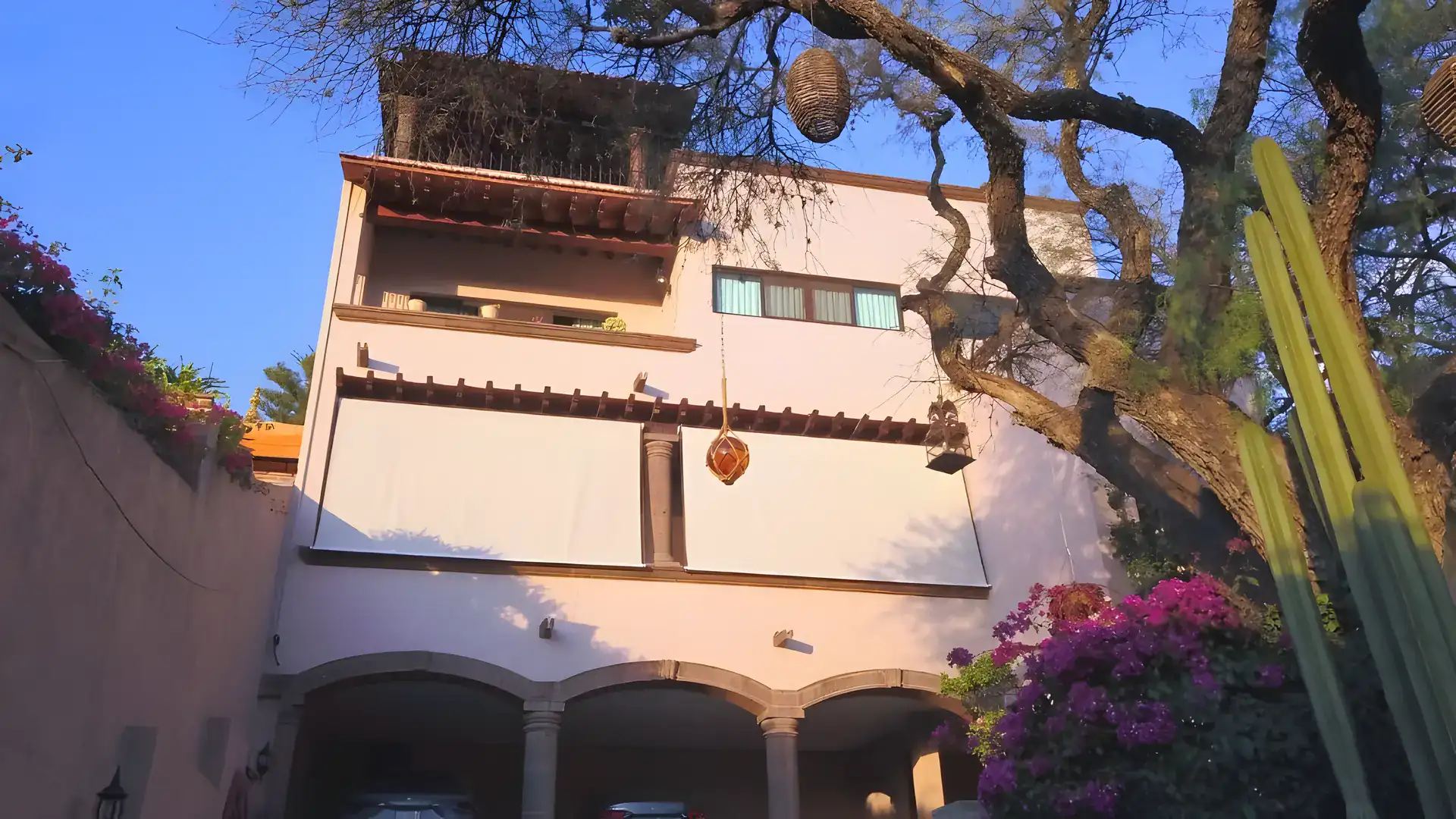 Casa Bellavista, two-story house with a rooftop terrace seen from the garden beside bougainvillea and a cactus, San Miguel de Allende