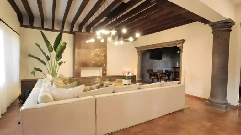 Casa Bellavista, living room with a cream sectional, a stone fireplace and a beamed ceiling with a light fixture, San Miguel de Allende