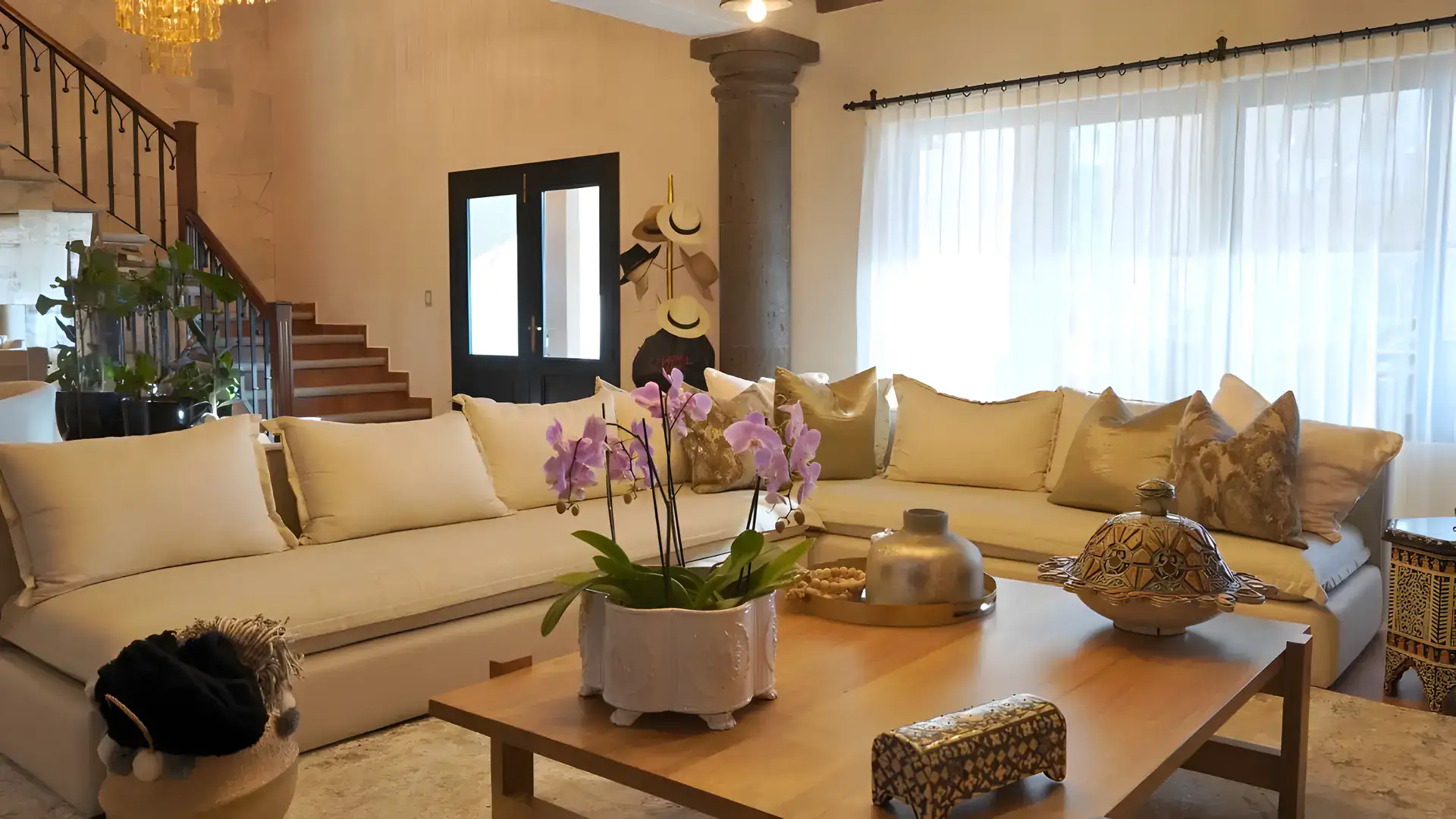 Casa Bellavista, living room with a sectional sofa, orchids on a wood coffee table and a staircase, San Miguel de Allende