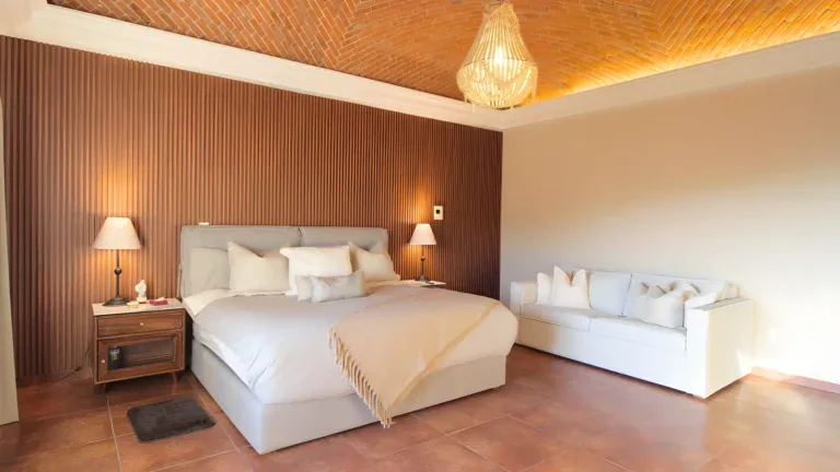 Casa Bellavista, bedroom with a slatted wood wall, a white bed and a brick vaulted ceiling with a beaded chandelier, San Miguel de Allende