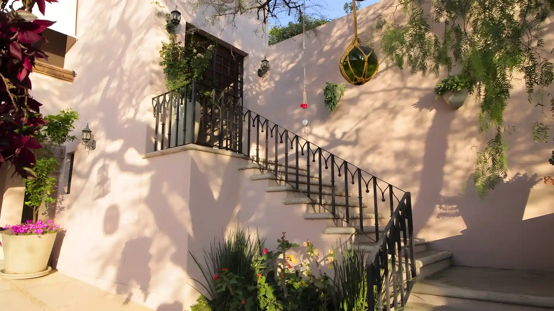 Casa Bellavista, exterior stairway with an iron railing, a balcony and flowering plants along a pink wall, San Miguel de Allende