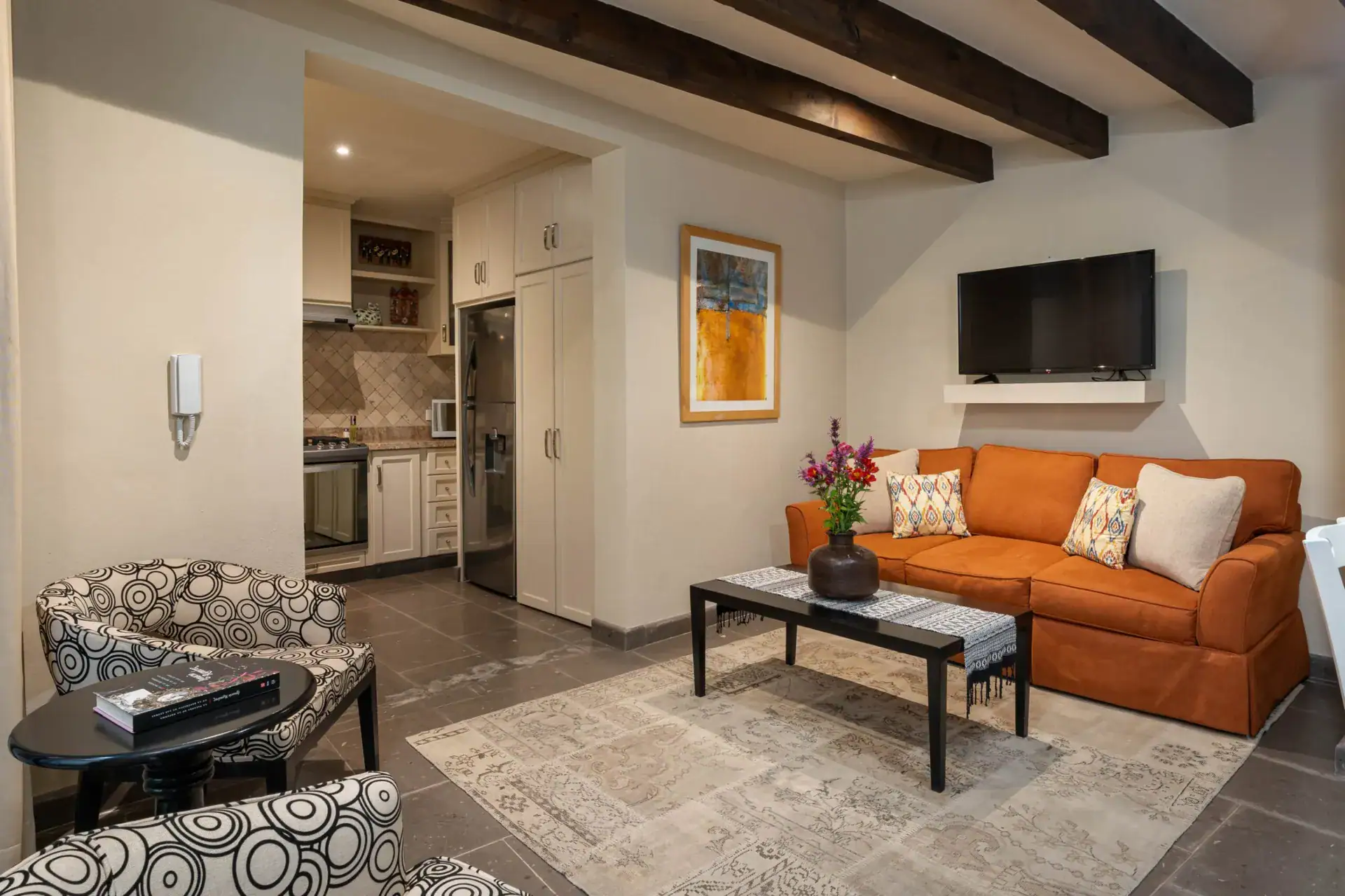Casa Biblioteca, unit living room with an orange sofa, patterned chairs, a television and a view to the kitchen, San Miguel de Allende