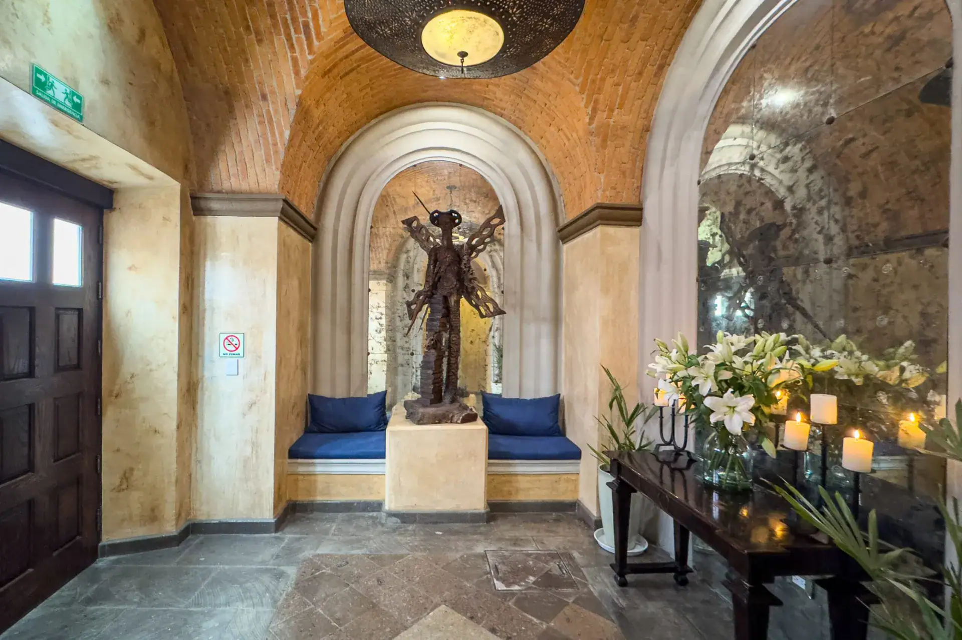 Casa Biblioteca, entry foyer with a brick vaulted ceiling, a winged sculpture in an arched niche and candles on a console, San Miguel de Allende