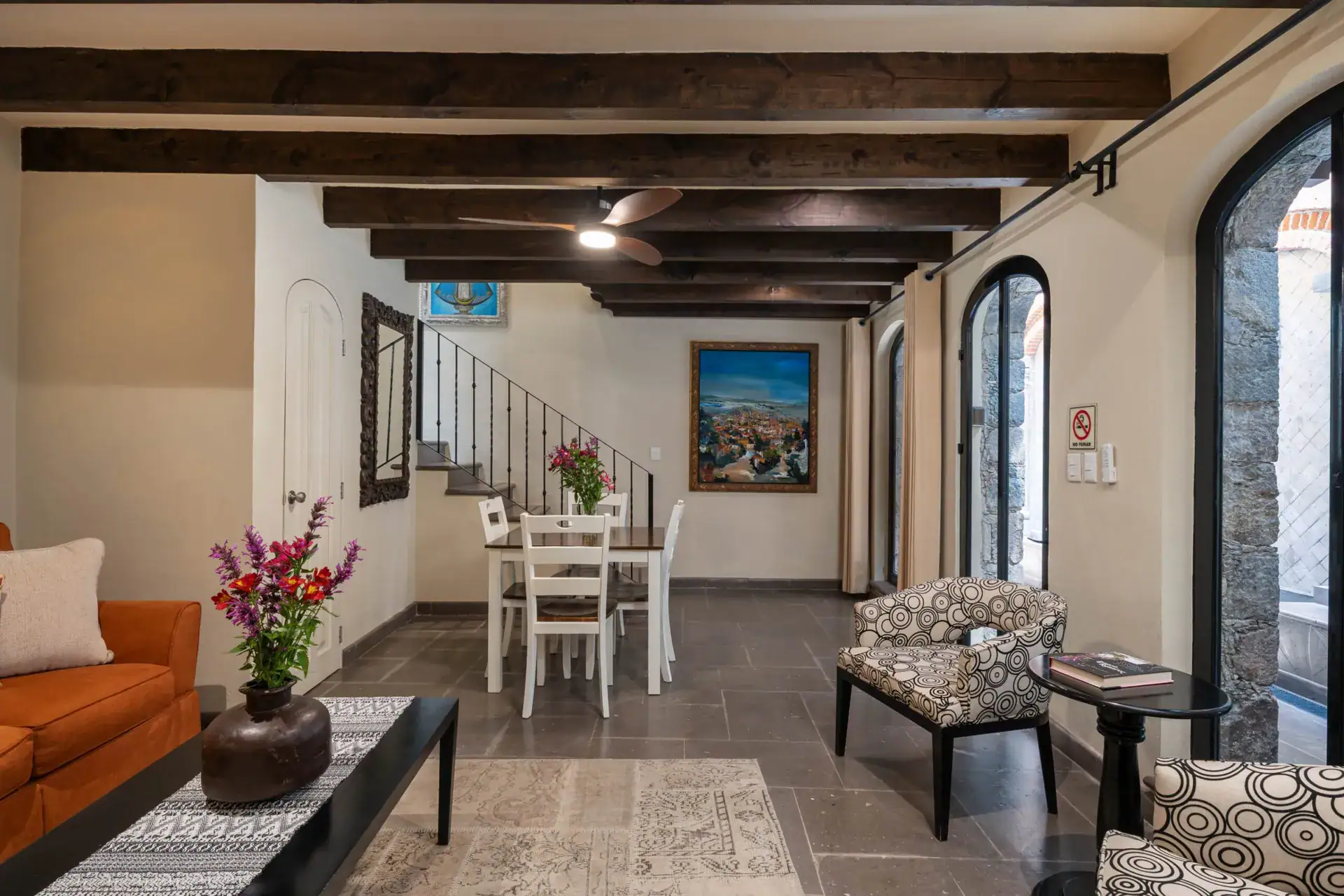 Casa Biblioteca, living and dining area with an orange sofa, white dining set and a stairway under a beamed ceiling, San Miguel de Allende