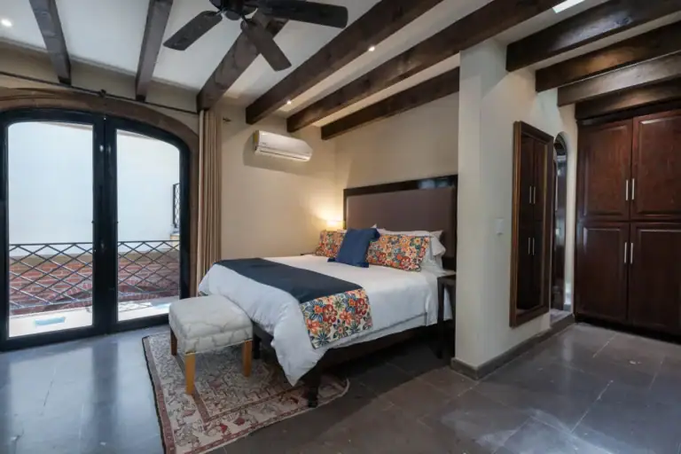 Casa Biblioteca, bedroom with an arched glass door, a bed with a floral runner and beamed ceiling, San Miguel de Allende