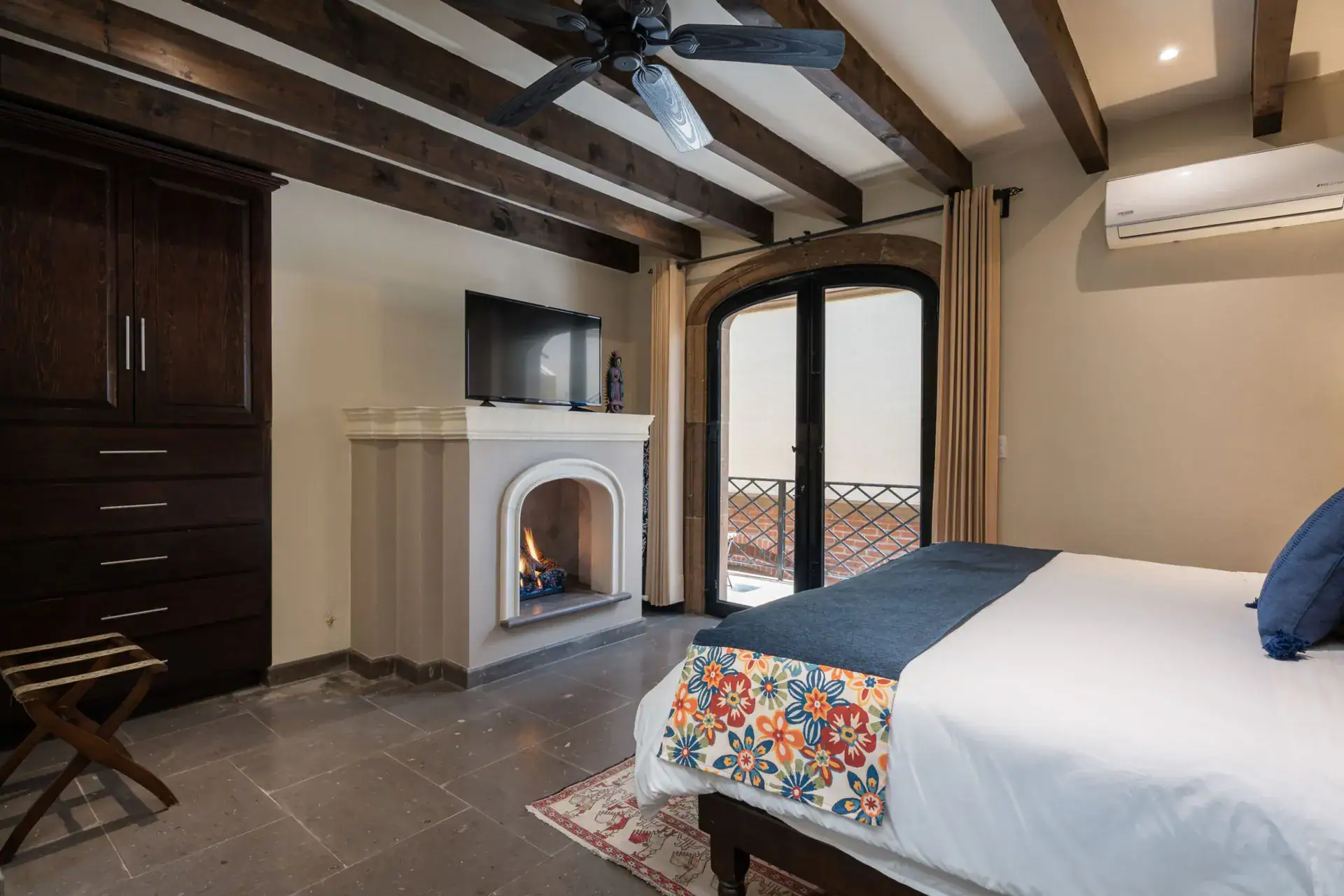 Casa Biblioteca, bedroom with a corner fireplace, television and arched glass doors to a balcony, San Miguel de Allende