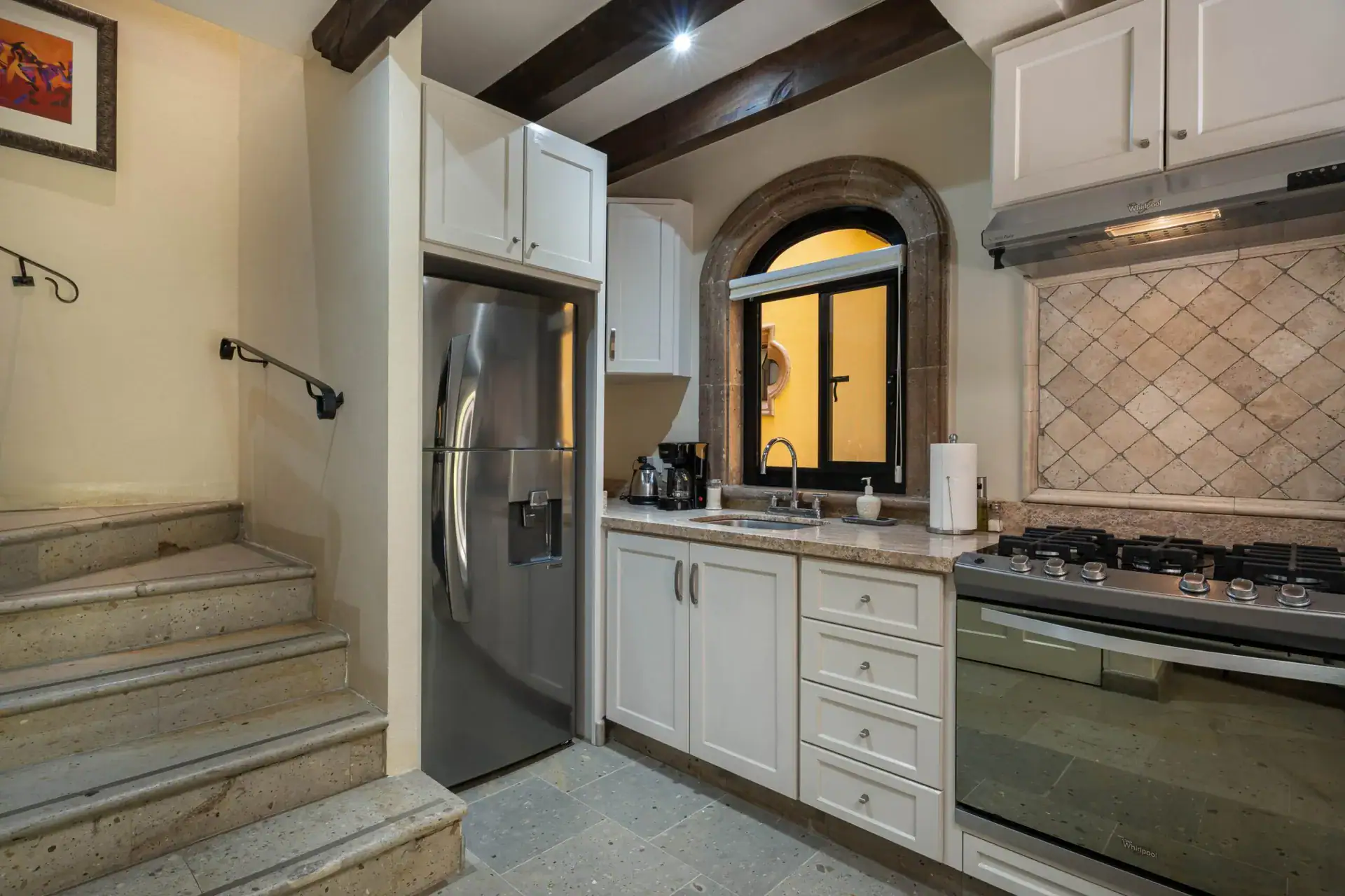 Casa Biblioteca, kitchen with white cabinets, an arched window and a stairway landing, San Miguel de Allende