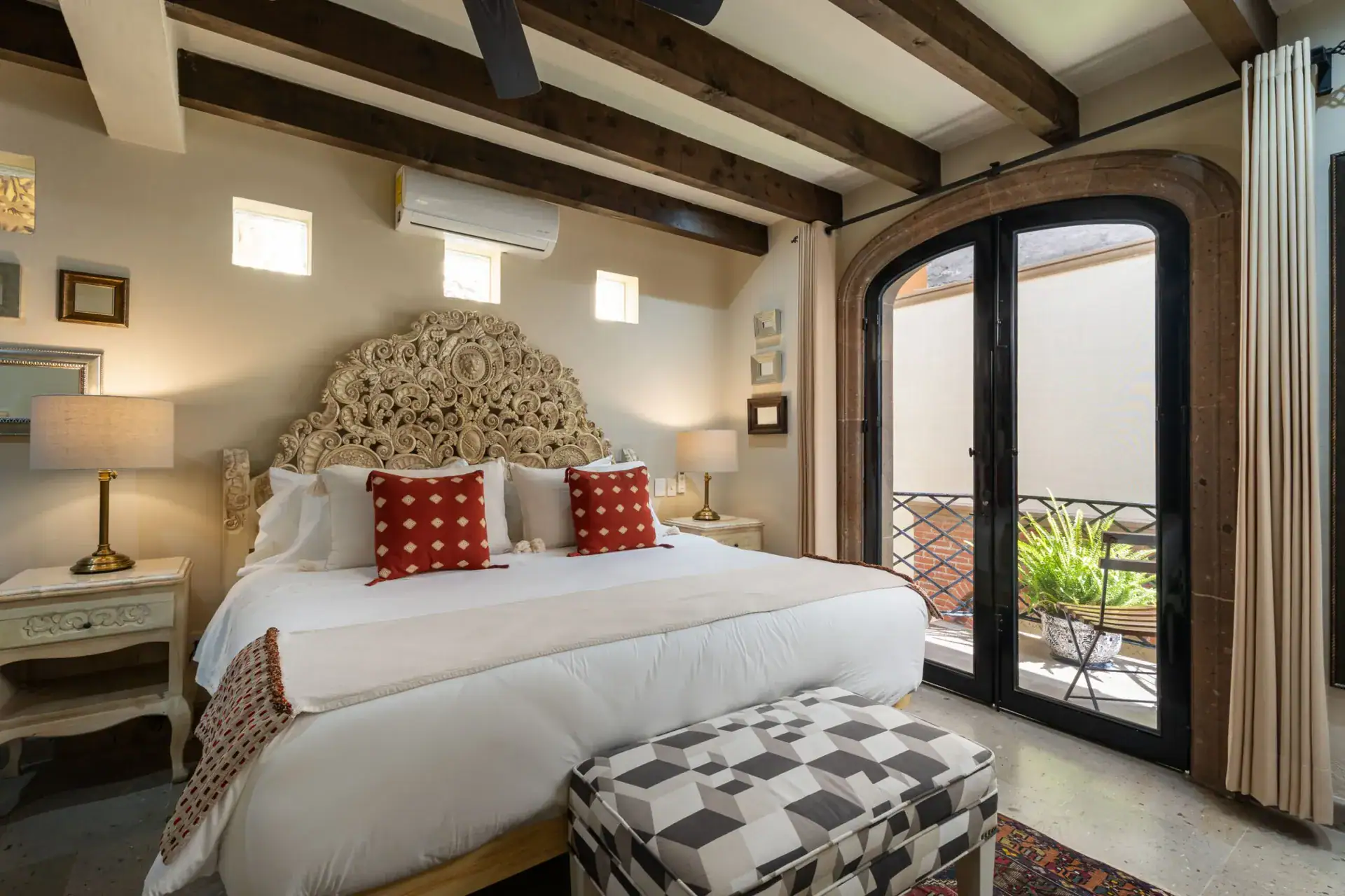 Casa Biblioteca, bedroom with a carved headboard, red accent pillows and a patterned bench, San Miguel de Allende