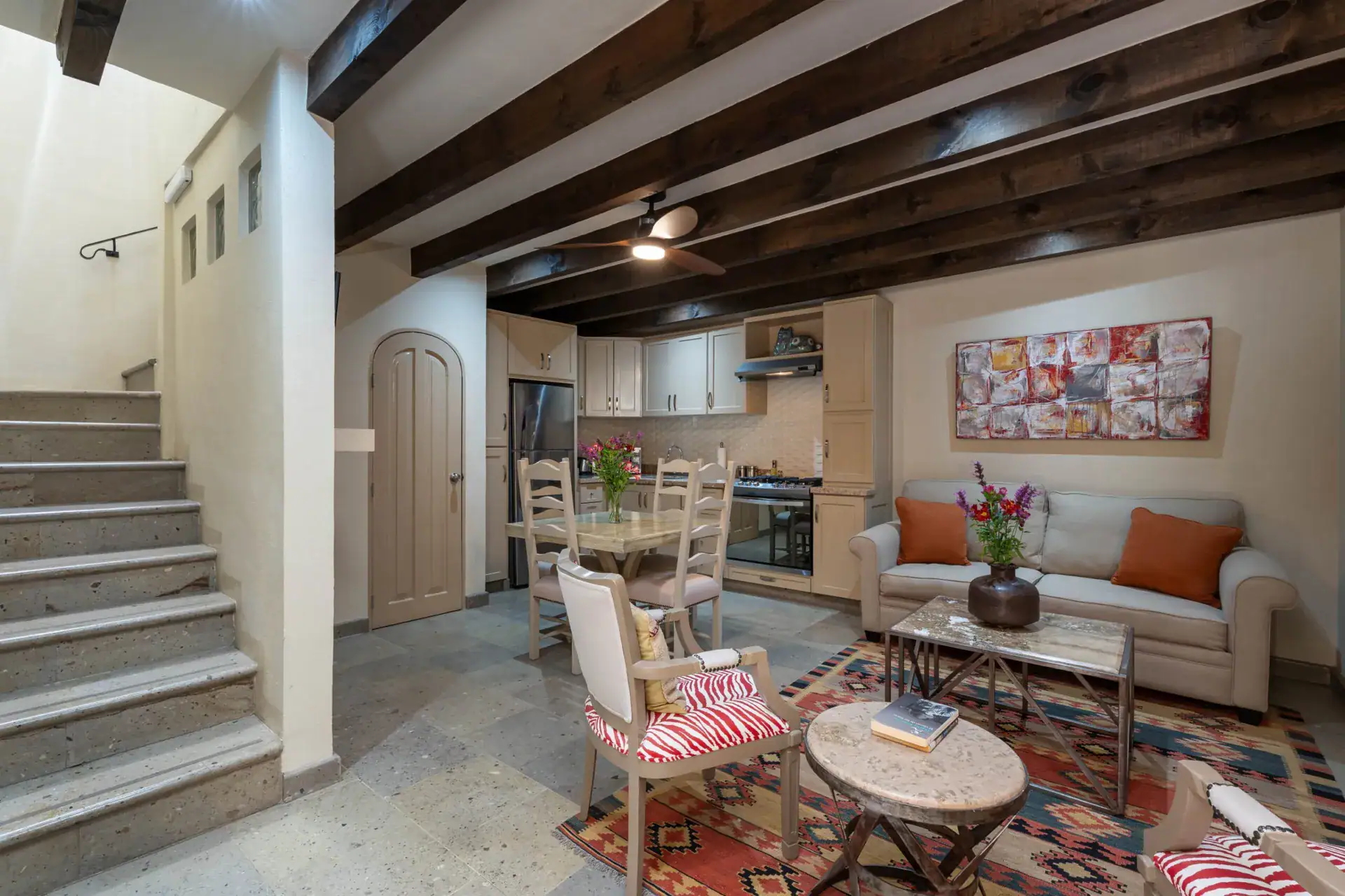 Casa Biblioteca, split-level living area with a staircase, sofa and kitchen under dark beams, San Miguel de Allende