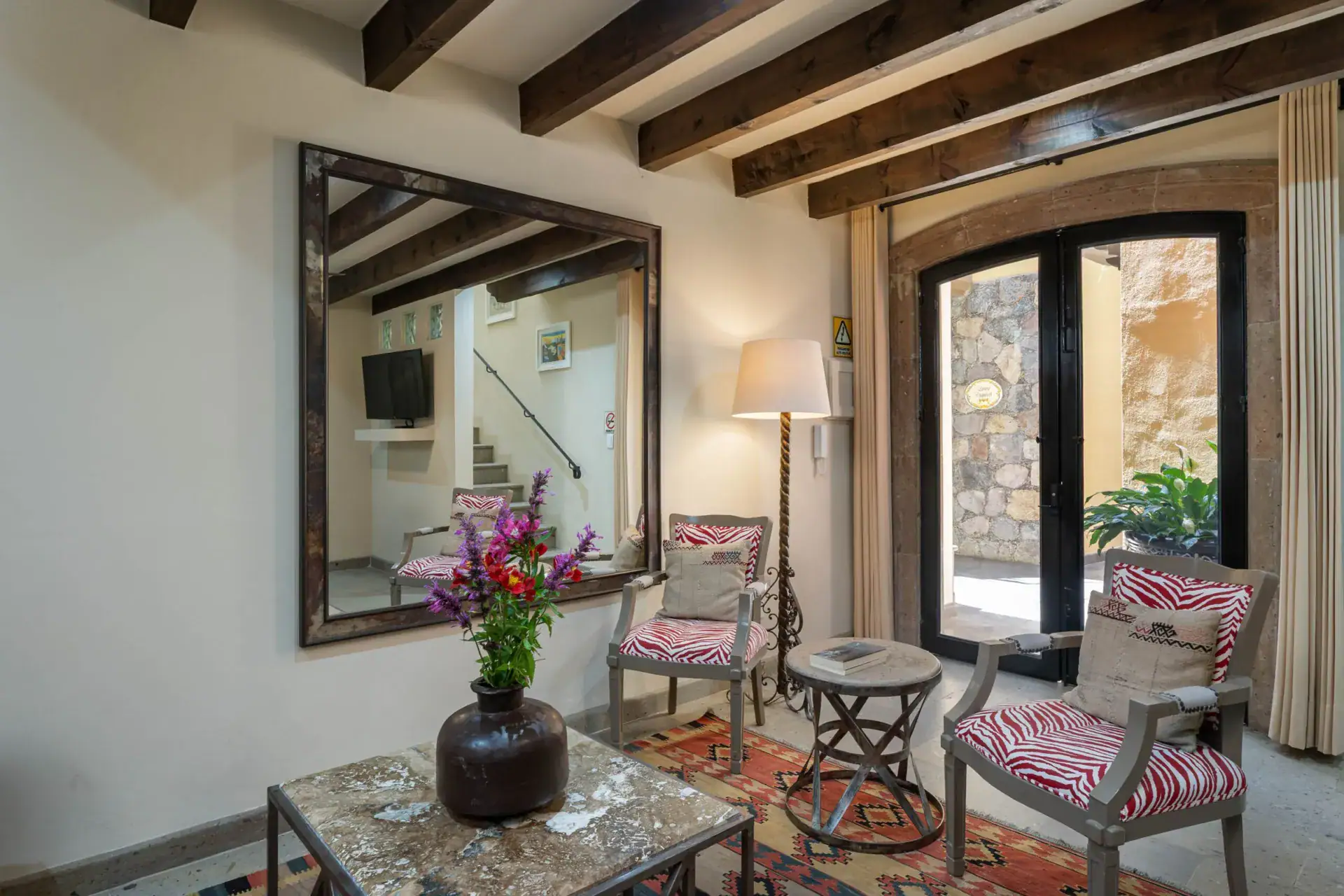 Casa Biblioteca, sitting area with a large mirror, striped armchairs and glass doors to the courtyard, San Miguel de Allende