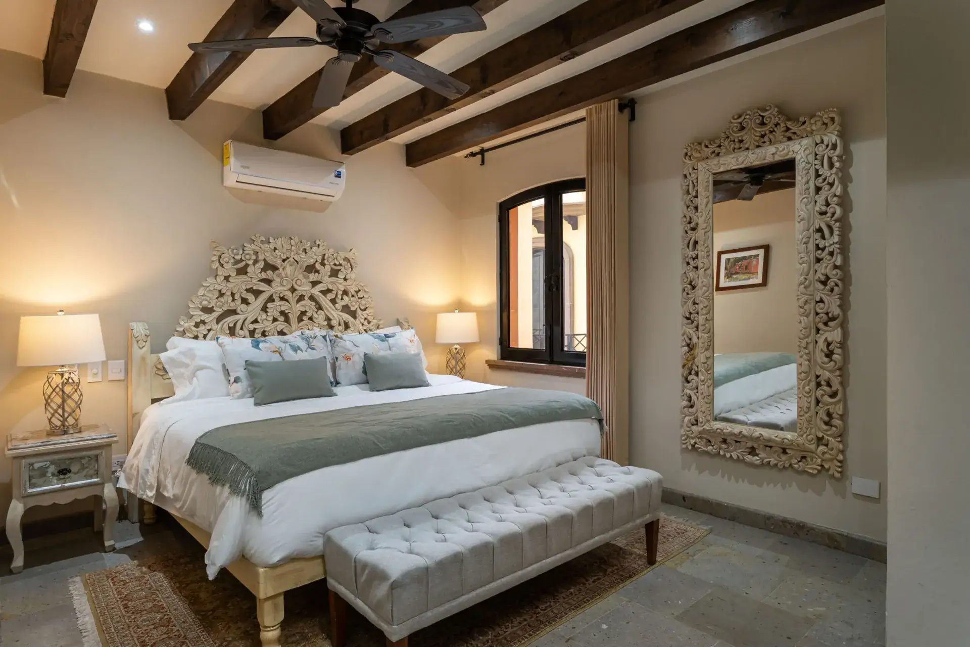 Casa Biblioteca, bedroom with a carved wood headboard, tufted bench and a tall carved mirror, San Miguel de Allende