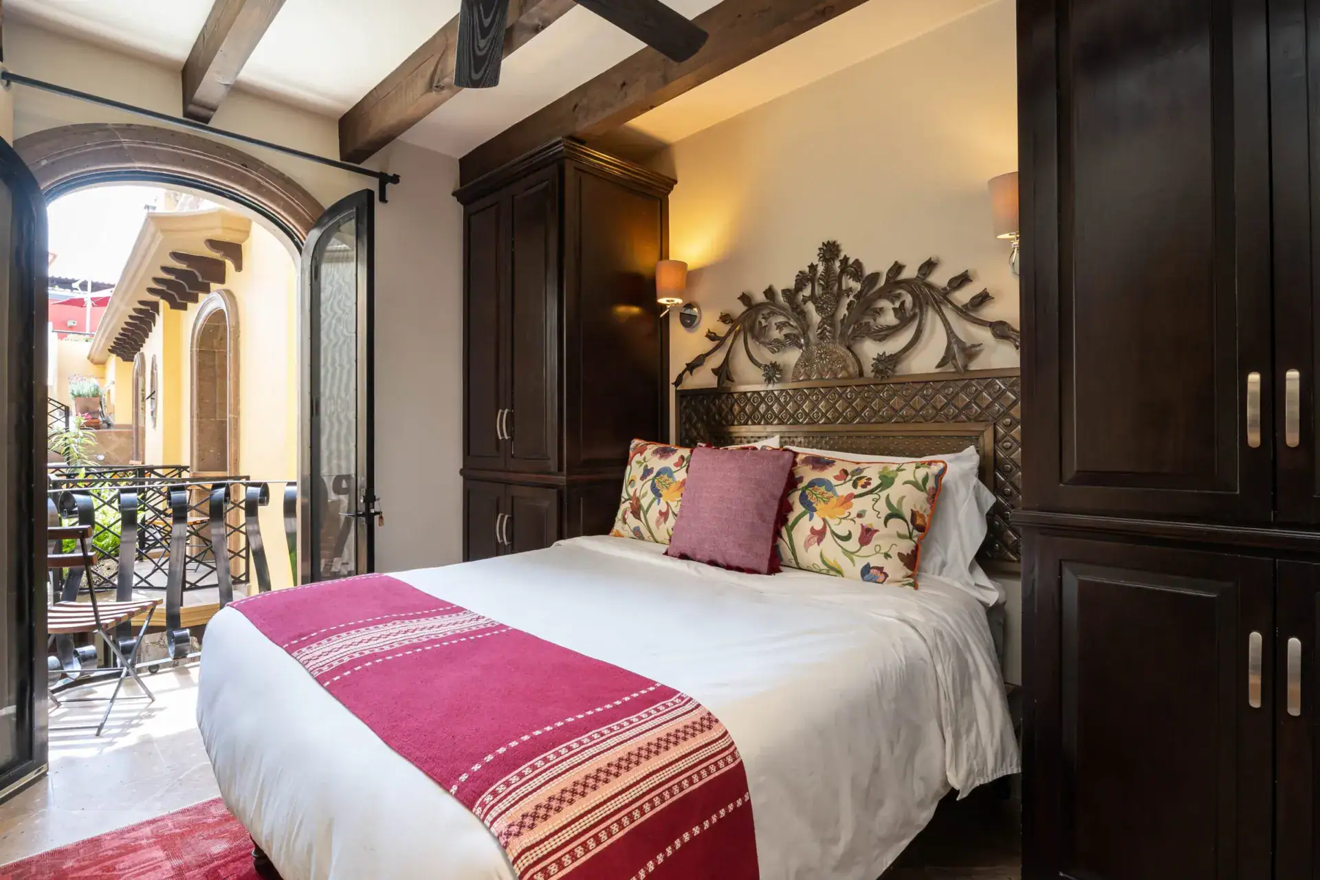 Casa Biblioteca, bedroom with a wrought-iron headboard, pink striped runner and an arched door to a balcony, San Miguel de Allende