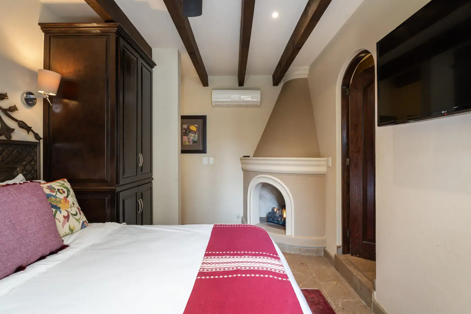 Casa Biblioteca, bedroom with a corner fireplace, carved headboard and a wall-mounted television, San Miguel de Allende