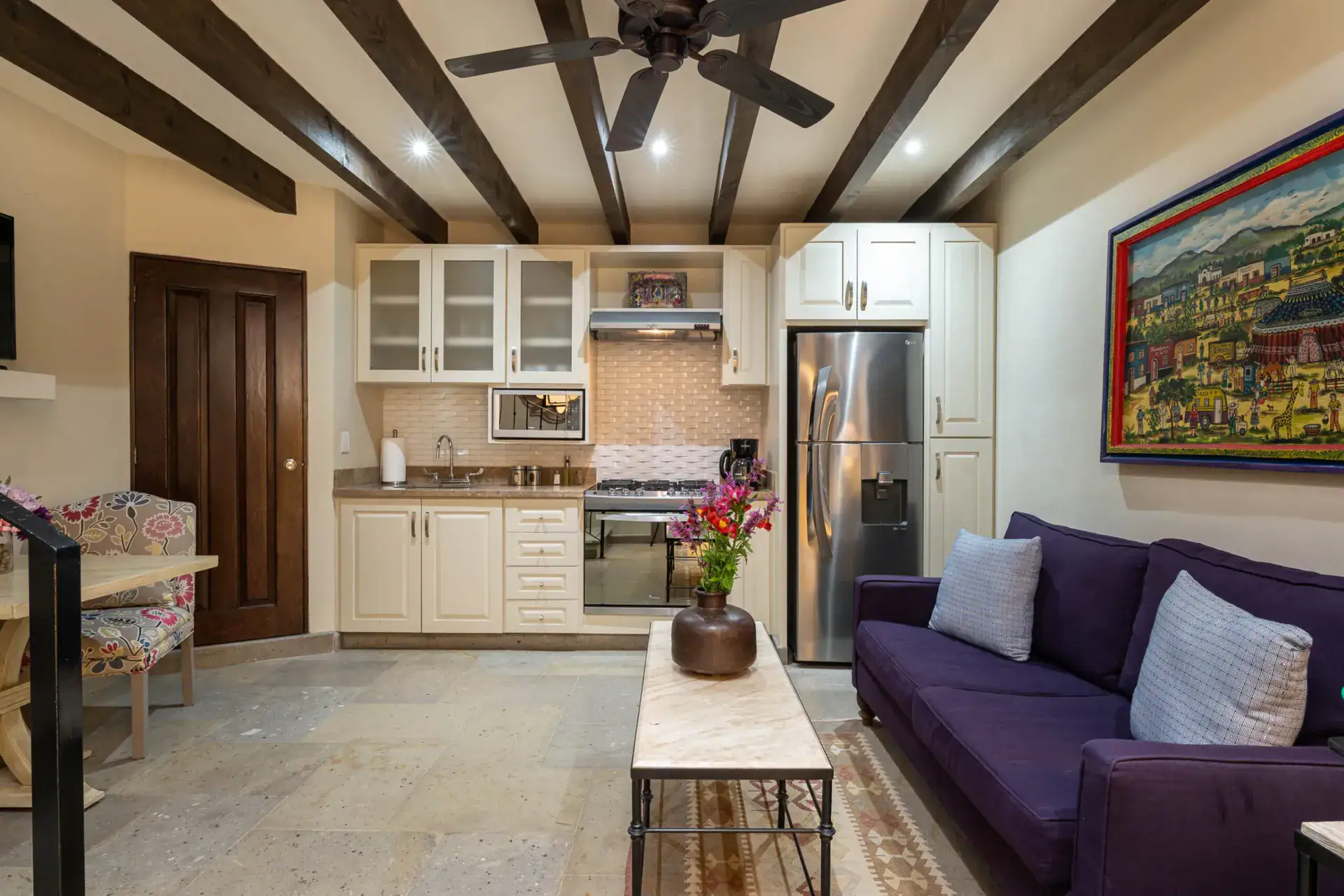 Casa Biblioteca, living area with a purple sofa, kitchenette and a large painted town scene, San Miguel de Allende