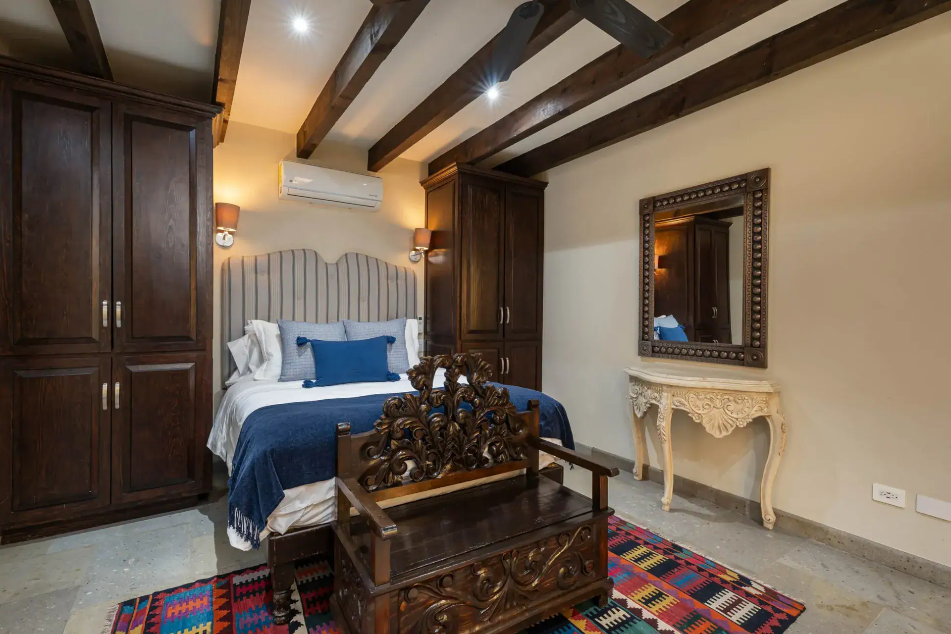 Casa Biblioteca, bedroom with a navy bedspread, carved bench and a dark wood armoire, San Miguel de Allende