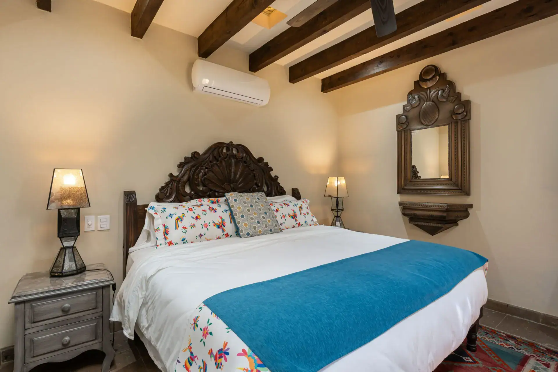 Casa Biblioteca, bedroom with a teal runner, carved headboard and a wall-mounted air conditioner, San Miguel de Allende