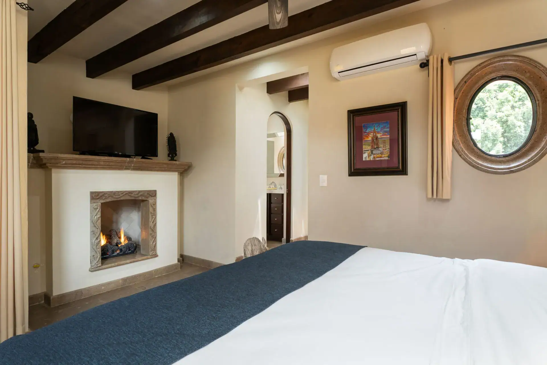 Casa Biblioteca, bedroom with a fireplace, round window and a navy bed runner, San Miguel de Allende