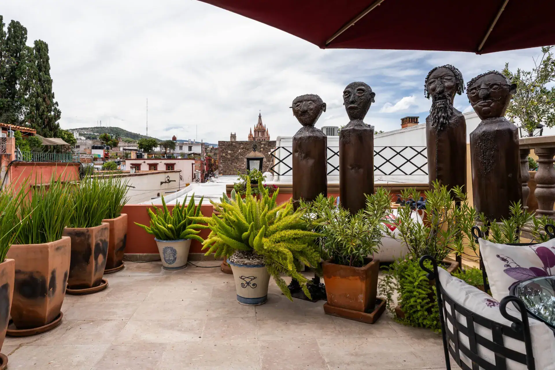 Casa Biblioteca, rooftop terrace with potted plants and carved wooden figures overlooking town, San Miguel de Allende