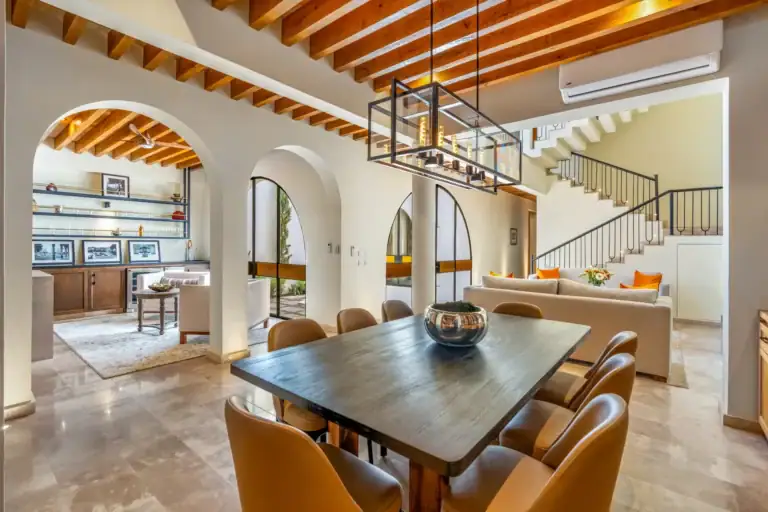 Casa Buenos Tiempos, dining table with tan chairs under a wood-beam ceiling and arched openings to the living area, San Miguel de Allende