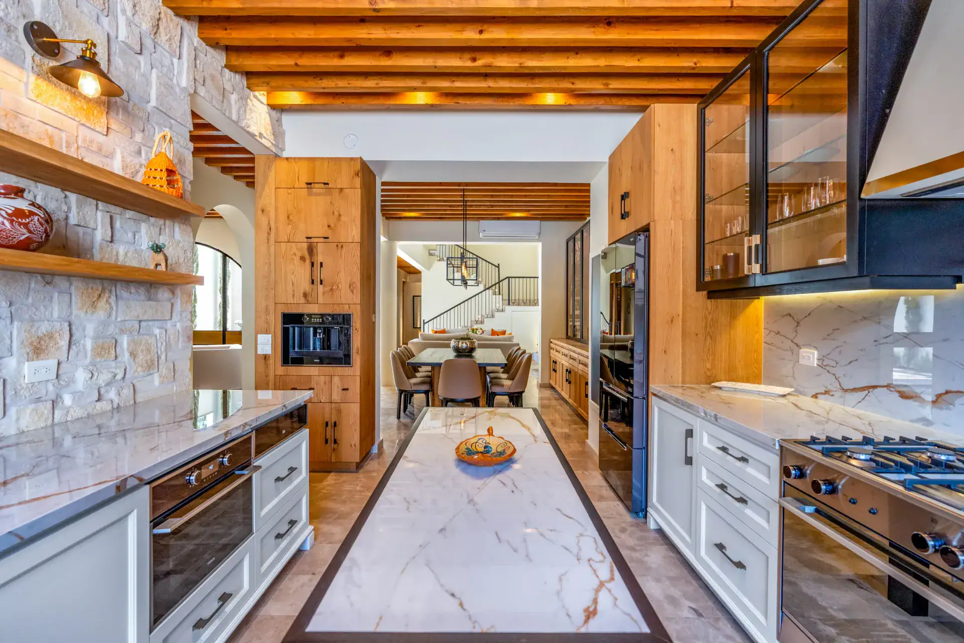 Casa Buenos Tiempos, galley kitchen with a marble-look island runner, stone wall, white cabinets and black-framed glass cabinets, San Miguel de Allende