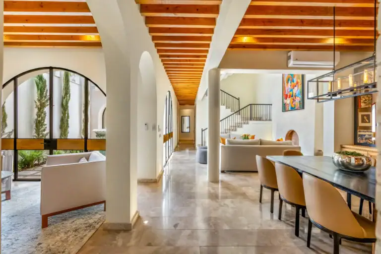 Casa Buenos Tiempos, open-plan dining and living area with a tall arched window and stairs, San Miguel de Allende