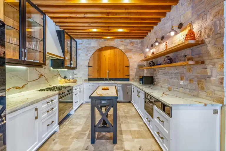 Casa Buenos Tiempos, kitchen with a quartz island, white cabinets, a stone feature wall and an arched wood door, San Miguel de Allende
