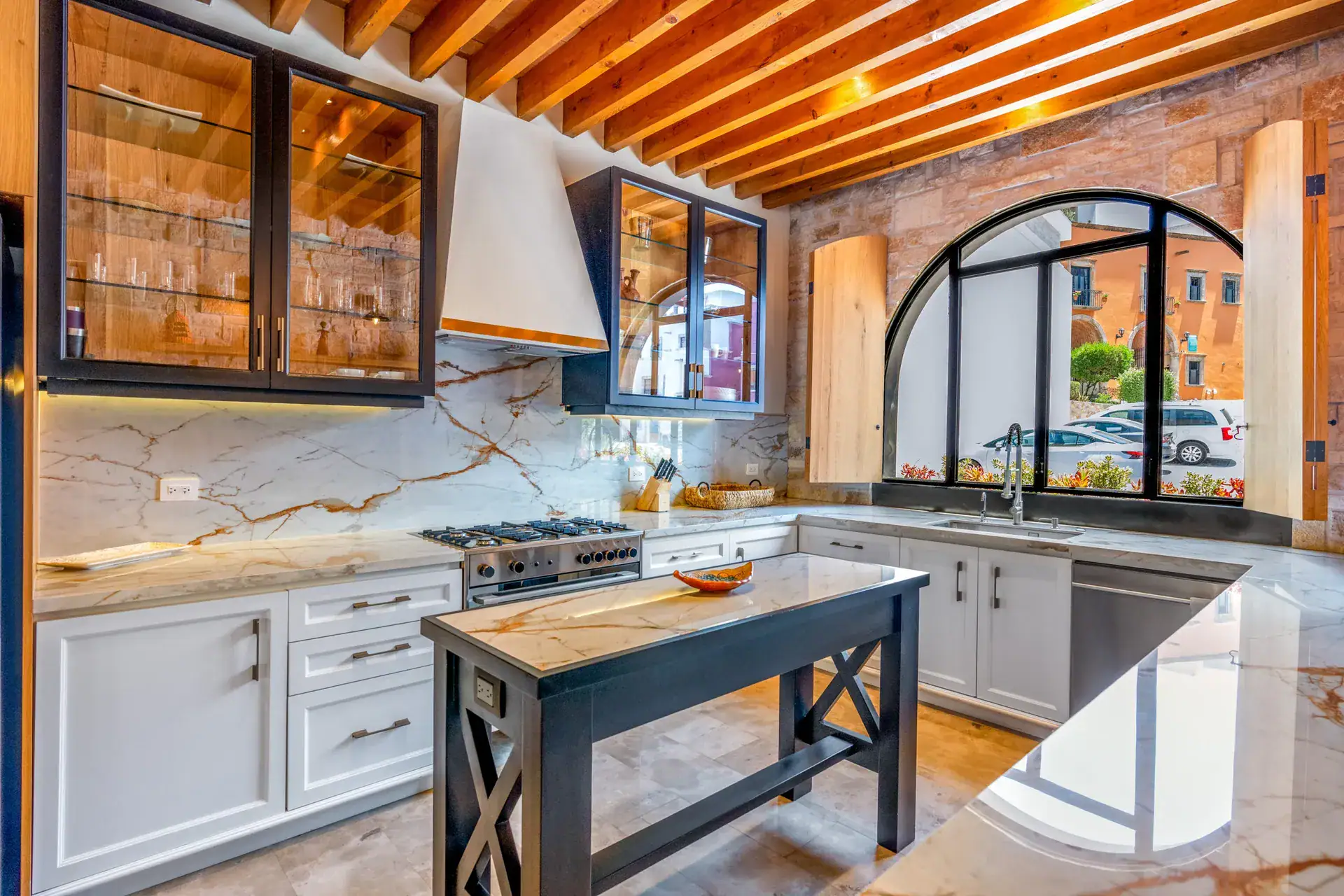 Casa Buenos Tiempos, kitchen with veined stone backsplash, a range, an island and an arched window, San Miguel de Allende