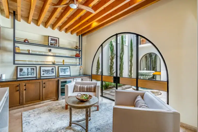 Casa Buenos Tiempos, sitting area with armchairs, a round table, shelves and a tall arched glass window, San Miguel de Allende