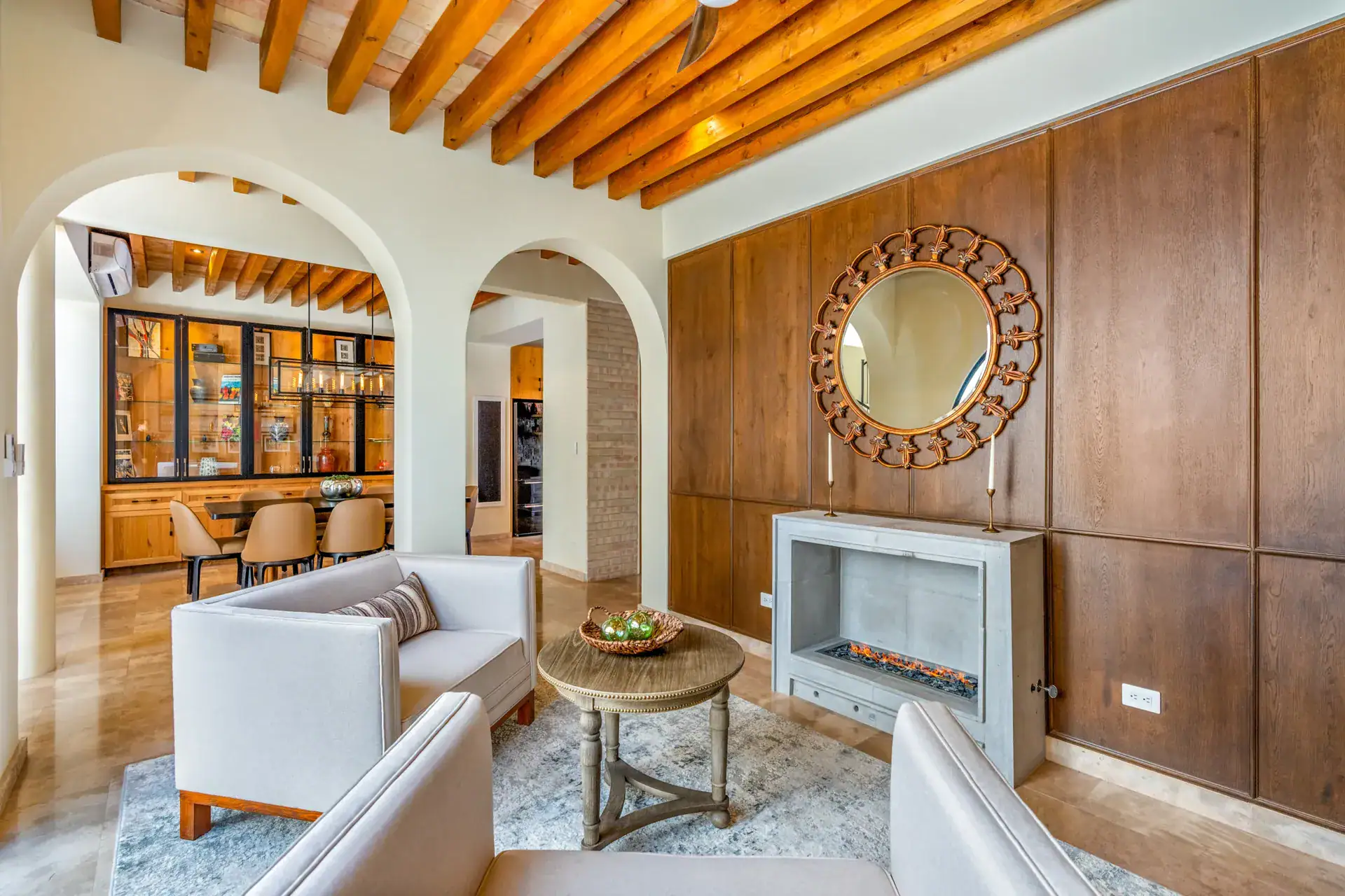 Casa Buenos Tiempos, living area with sofas facing a wood-paneled fireplace wall and a round mirror, San Miguel de Allende