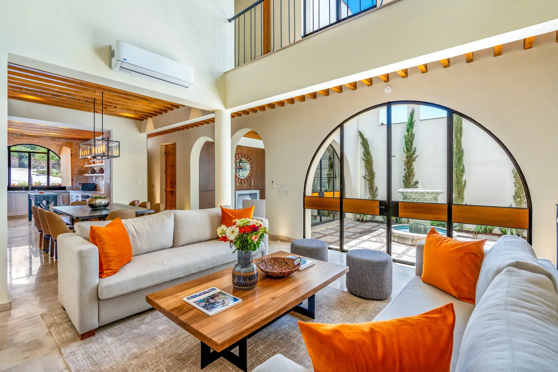 Casa Buenos Tiempos, double-height living room with an arched window wall, orange cushions and a wood coffee table, San Miguel de Allende