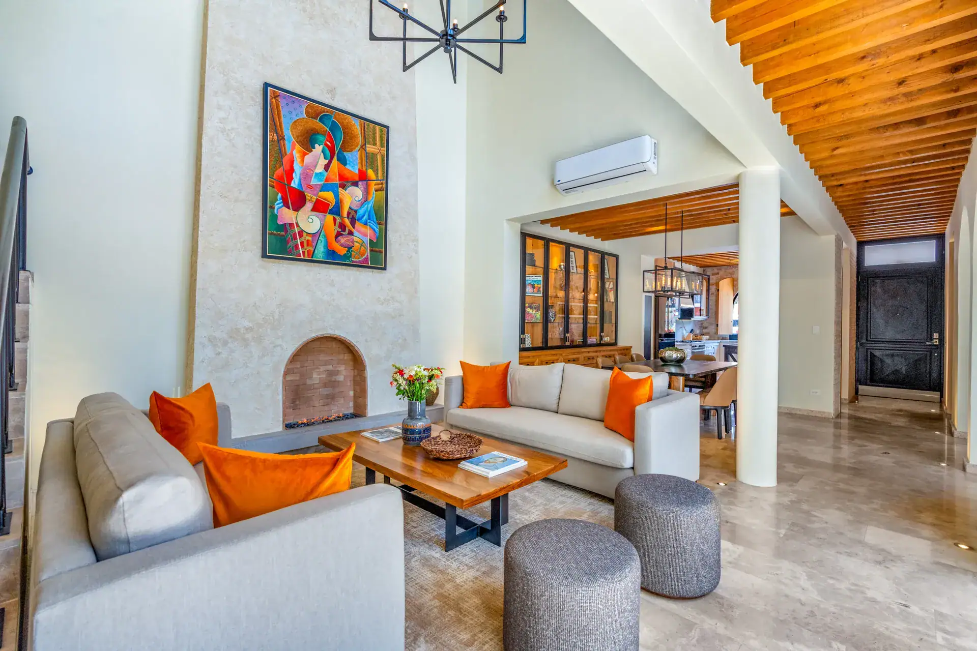 Casa Buenos Tiempos, living room with a fireplace nook, a colorful painting and stairs under wood beams, San Miguel de Allende