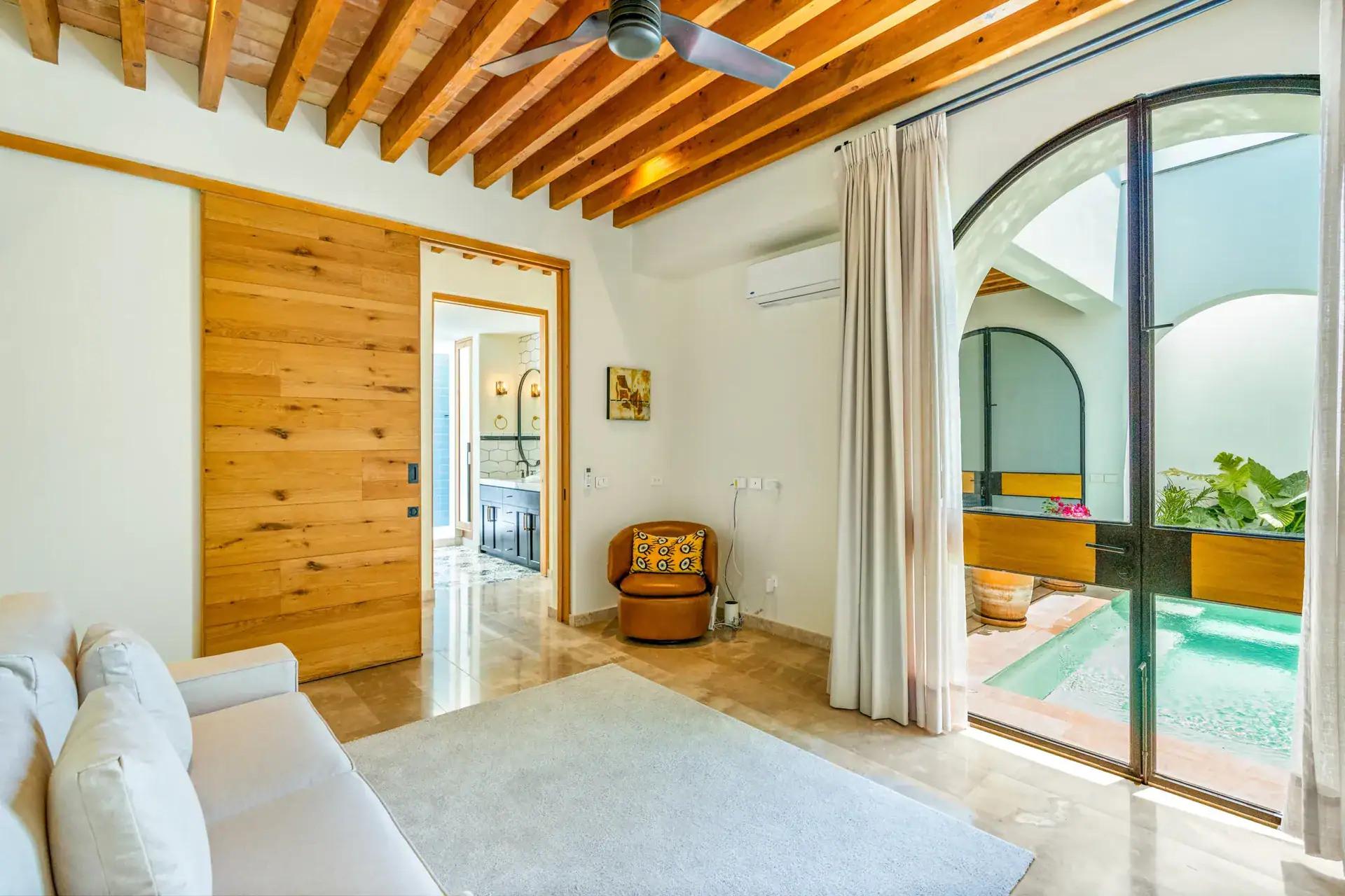 Casa Buenos Tiempos, bedroom with a sliding wood door, a sofa and arched glass doors to a plunge pool, San Miguel de Allende