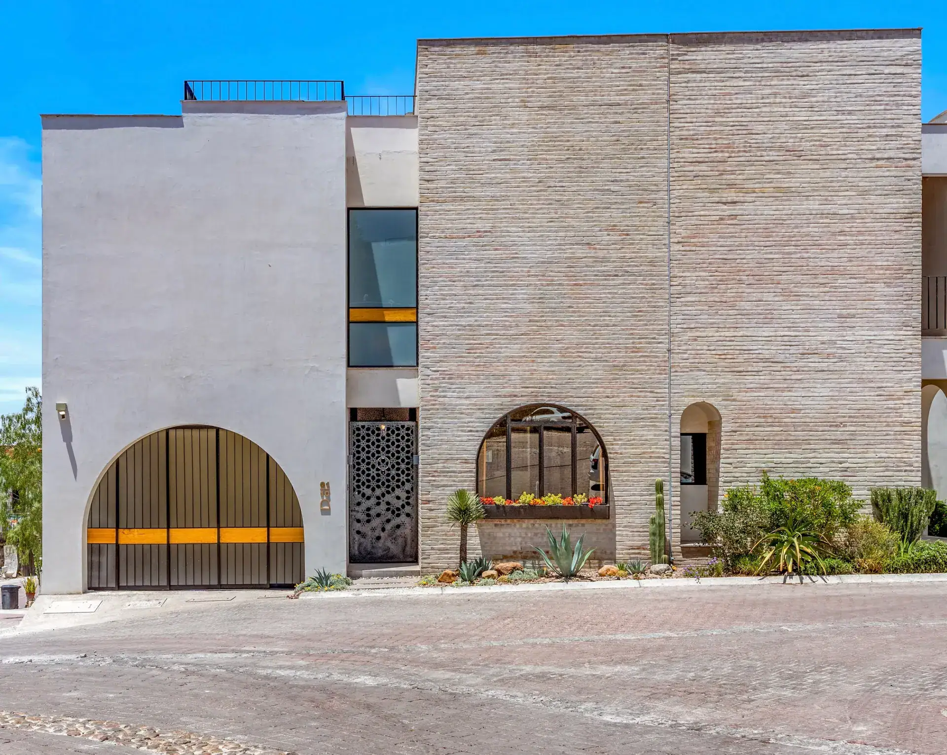 Casa Buenos Tiempos, modern house exterior with a stone-clad tower, arched garage door and an arched window, San Miguel de Allende
