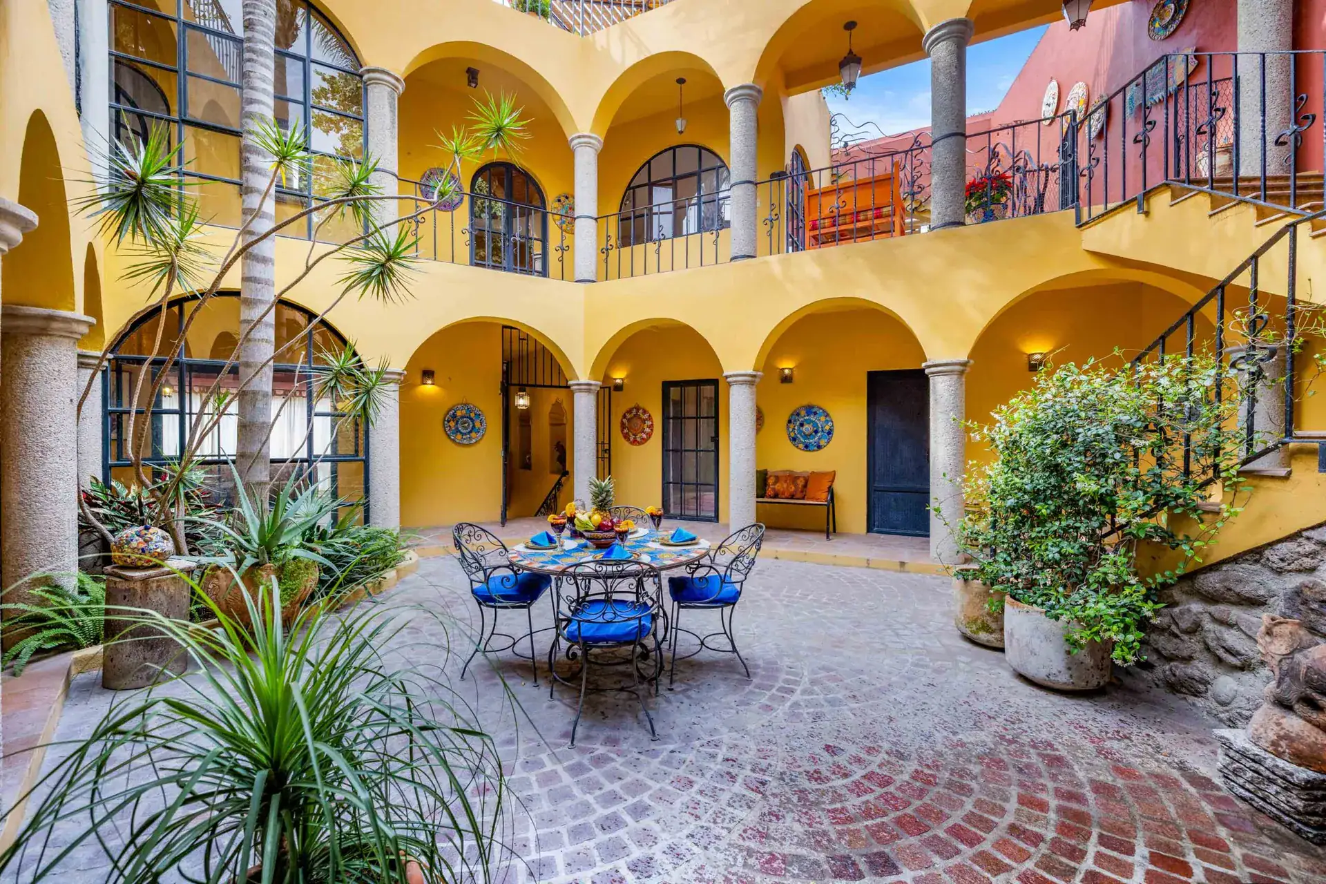 Casa Caracol Rojo, two-story yellow courtyard with arcades and a bistro table, San Miguel de Allende