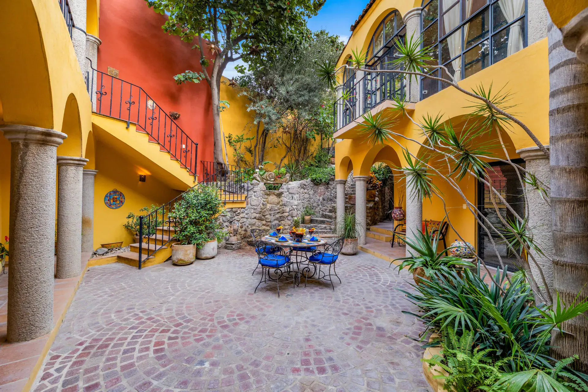 Casa Caracol Rojo, courtyard with a red staircase and a round mosaic table, San Miguel de Allende