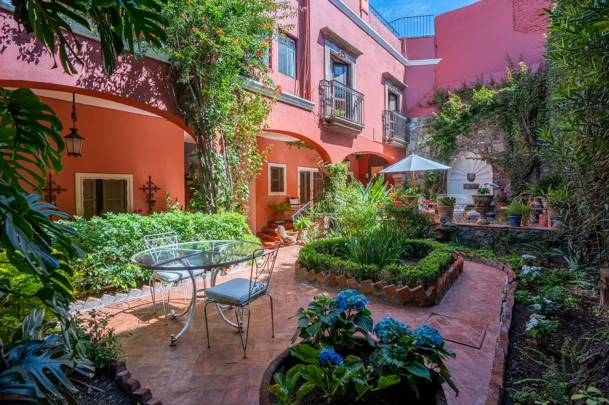 Casa Carolina, interior garden with a table and trimmed hedges beside the red house, San Miguel de Allende