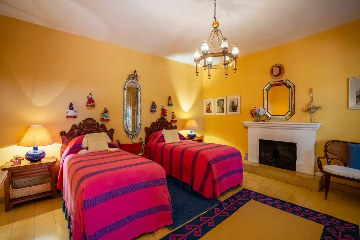 Casa Carolina, bedroom with two beds, red blankets and a white fireplace, San Miguel de Allende