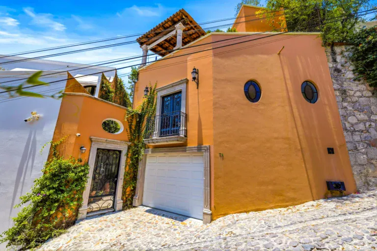 Casa Cascada, orange house facade with round windows, a white garage door and a wrought-iron gate on a cobblestone street, San Miguel de Allende