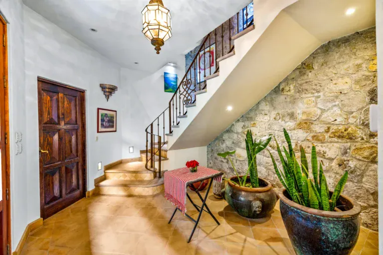 Casa Cascada, entry foyer with a carved wood door, a stone wall, a staircase with an iron railing and potted plants, San Miguel de Allende