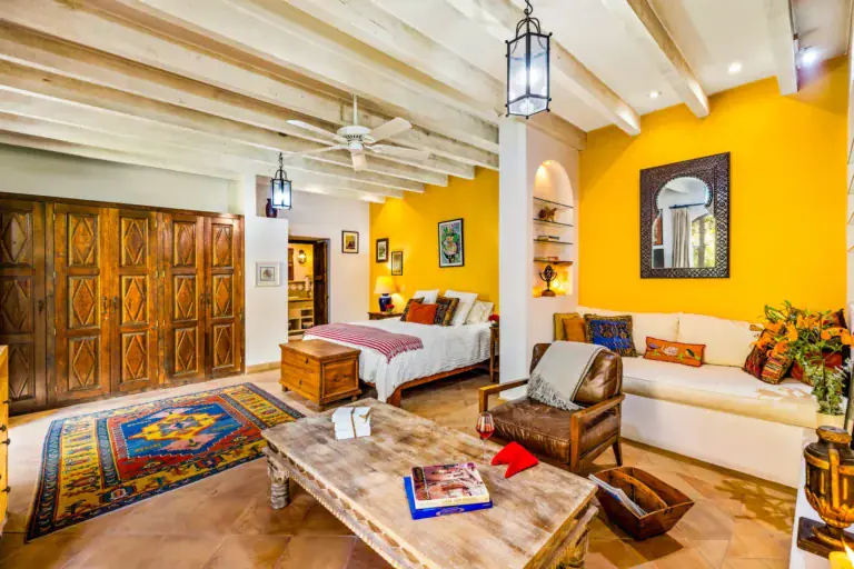 Casa Cascada, guest suite with a yellow wall, a wood armoire, a white sofa and a wood chest at the foot of the bed, San Miguel de Allende
