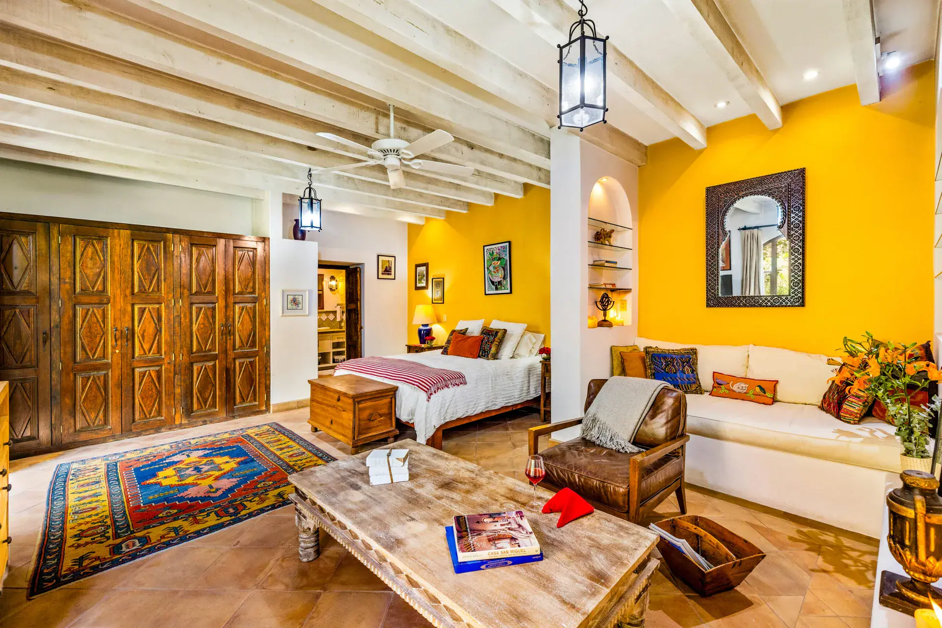 Casa Cascada, guest suite with a yellow wall, a wood armoire, a white sofa and a wood chest at the foot of the bed, San Miguel de Allende