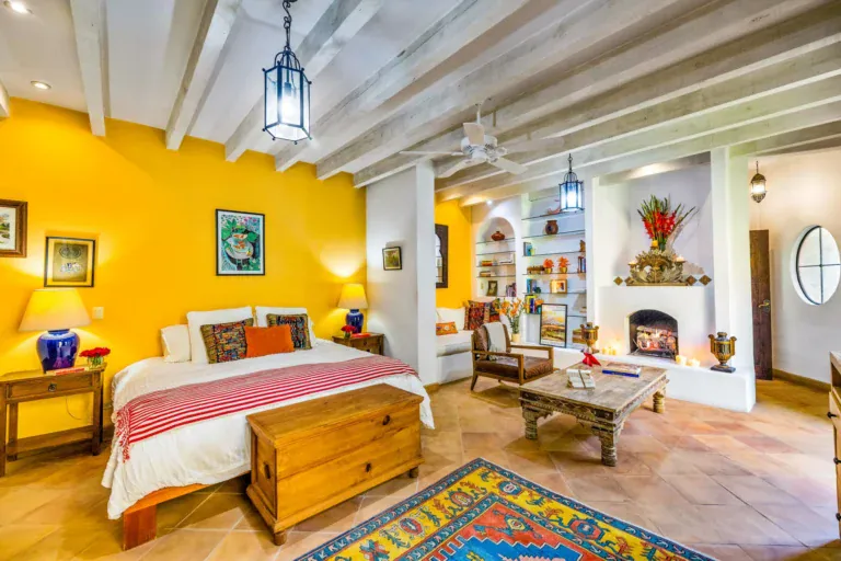 Casa Cascada, guest suite with a fireplace, a wood coffee table, a bed with a red striped throw and a Persian rug, San Miguel de Allende
