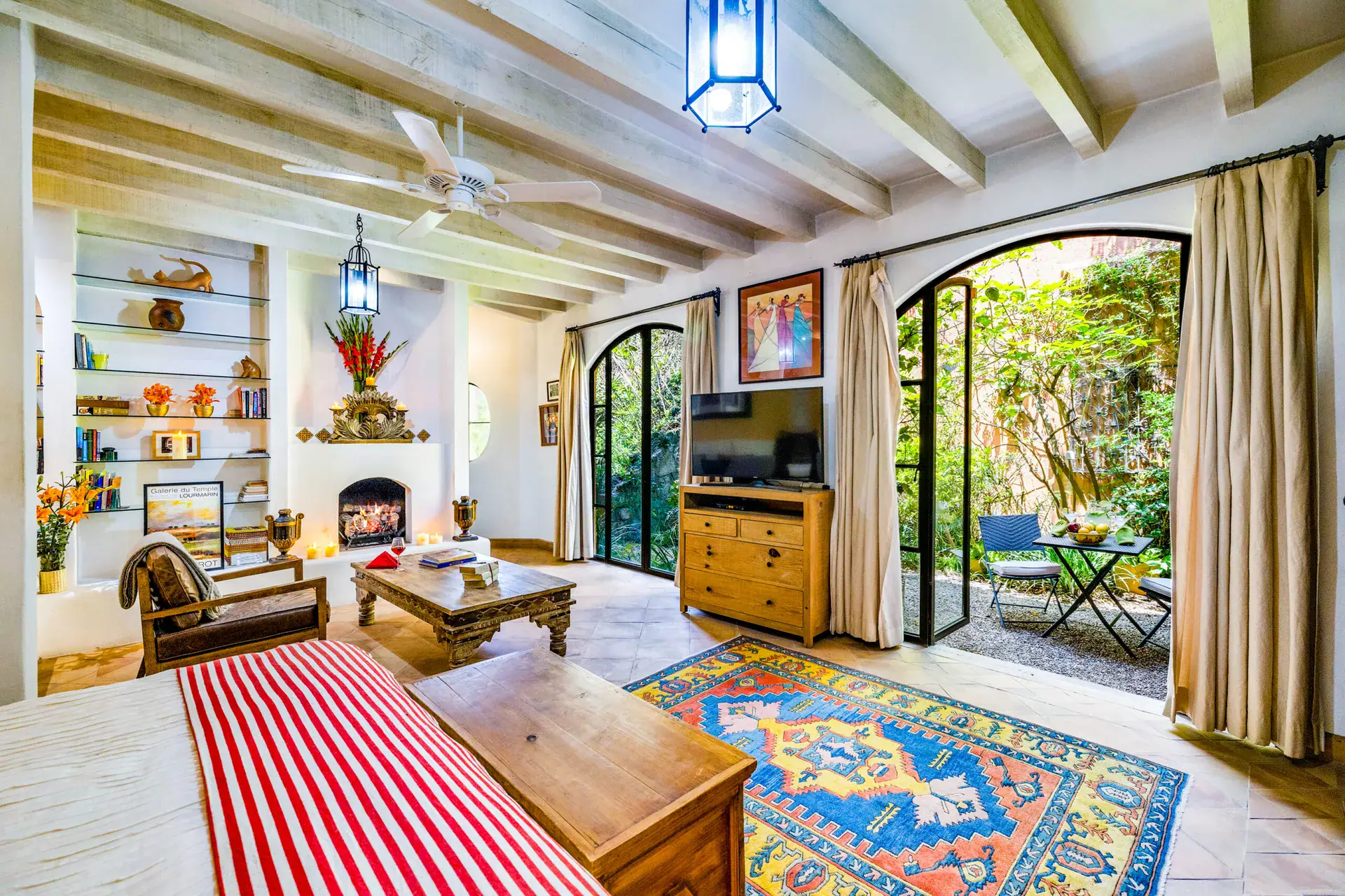 Casa Cascada, guest suite living area with arched glass doors to a garden, a fireplace and shelves, San Miguel de Allende