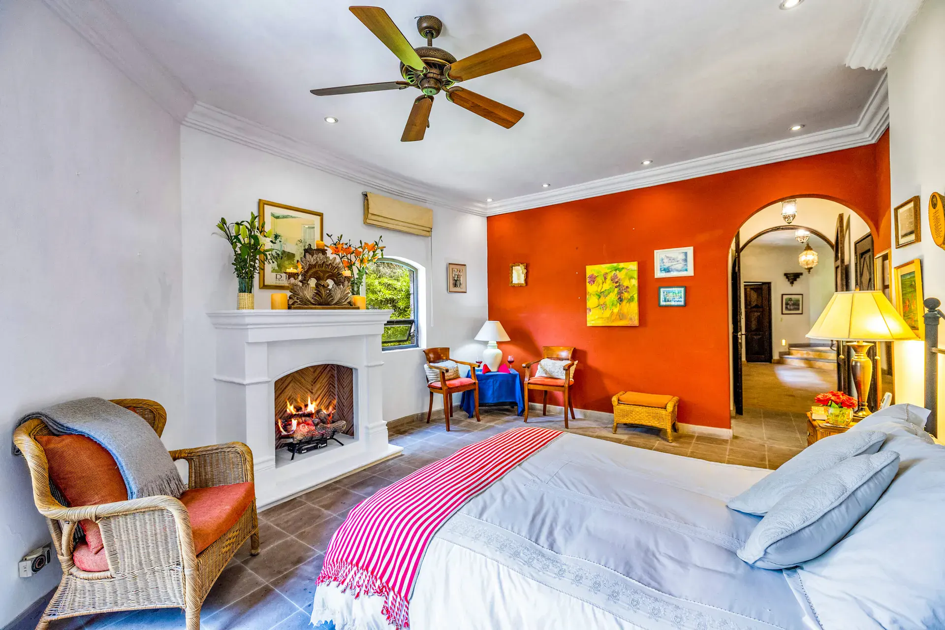 Casa Cascada, bedroom with a white fireplace, a red accent wall, a wicker armchair and a red striped throw, San Miguel de Allende