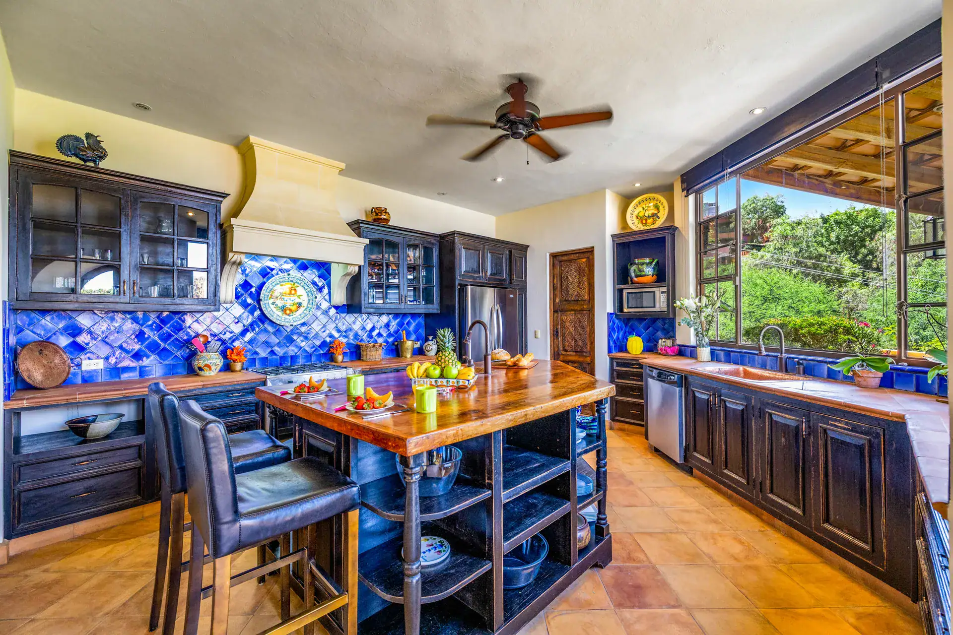 Casa Cascada, kitchen with dark blue cabinets, blue Talavera tile, a wood-topped island and a view of the hillside, San Miguel de Allende